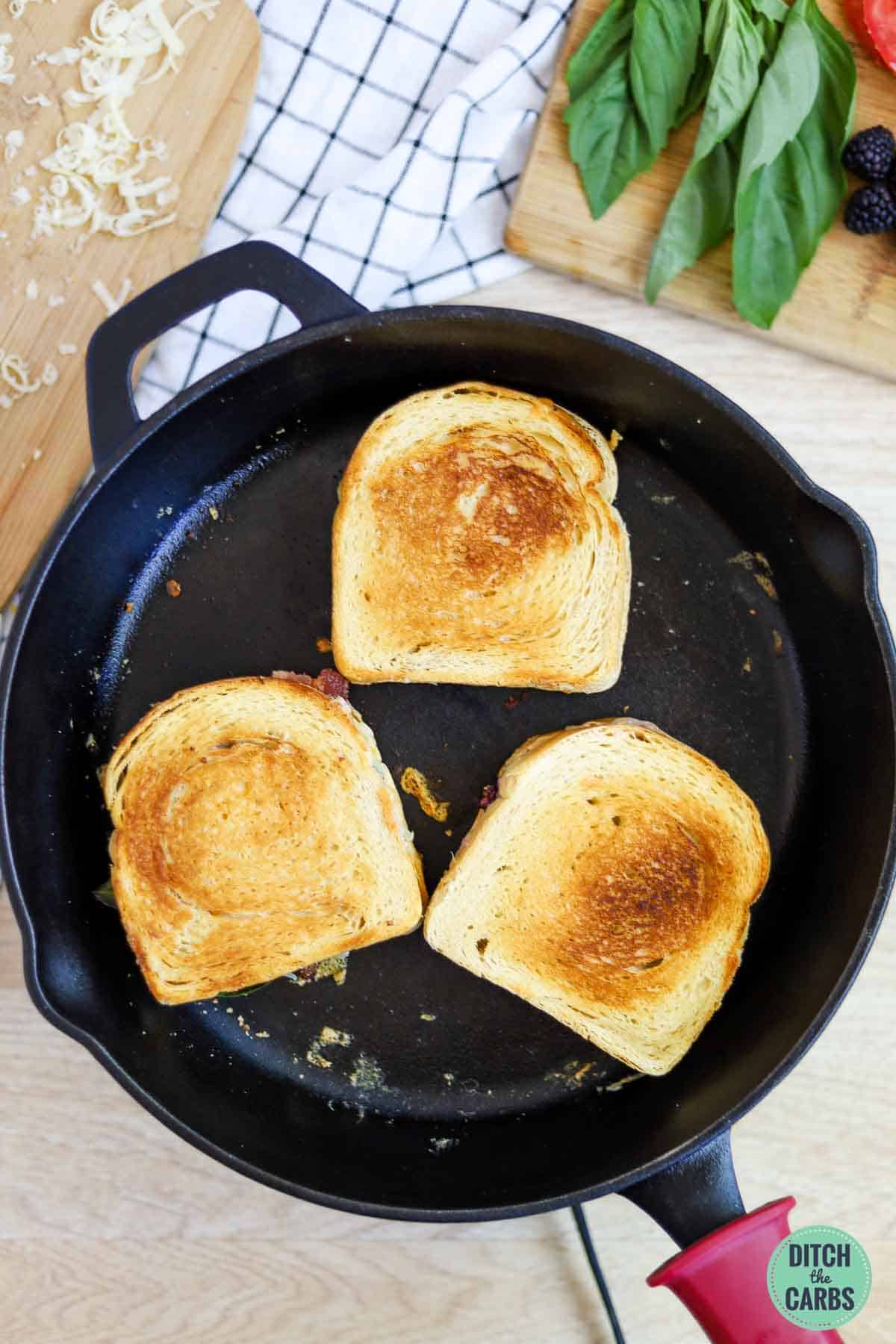 Three grilled cheese sandwiches cooking in a cast iron skillet.