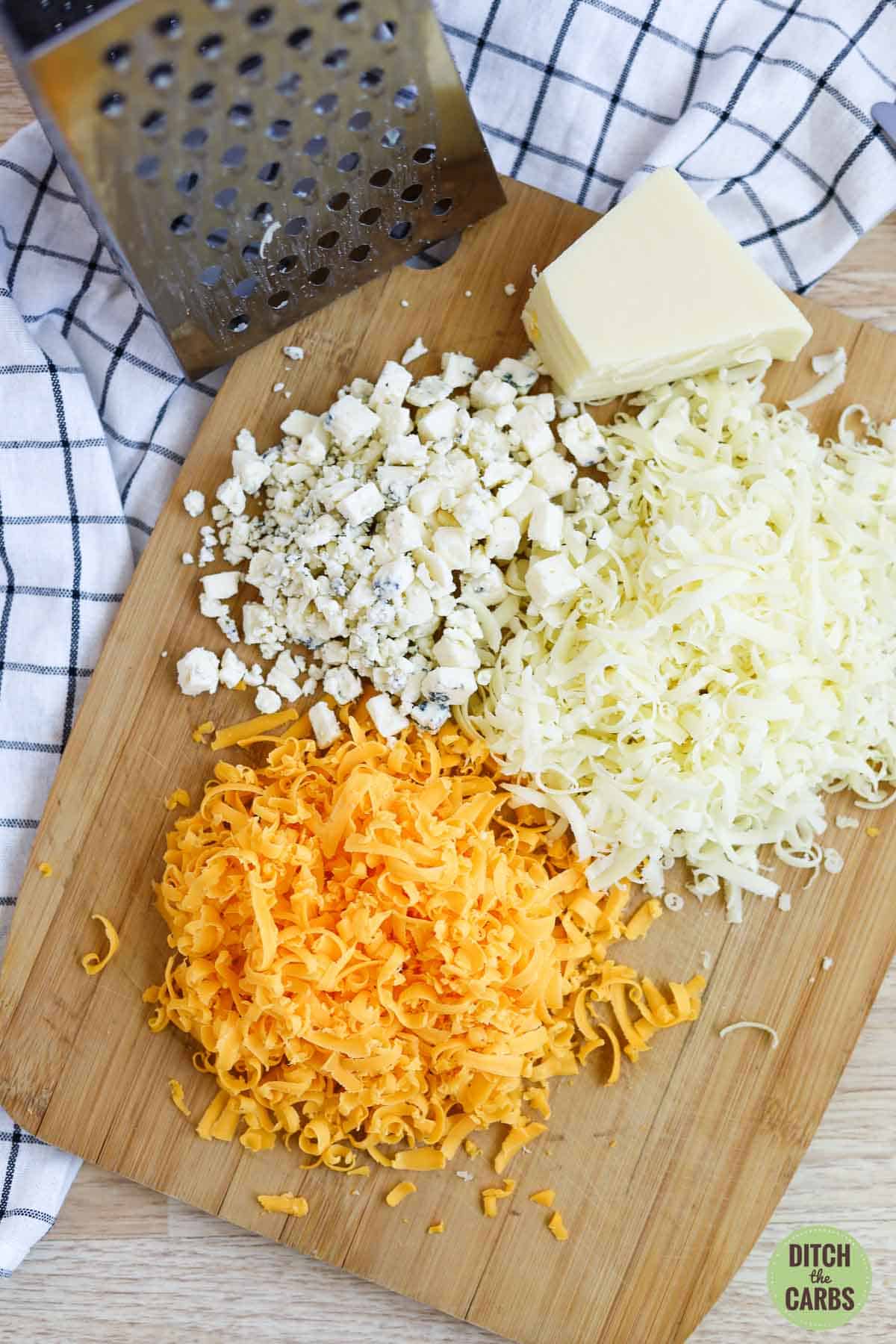 Cheddar, mozzarella, and blue cheese shredded and crumbled on a cutting board.