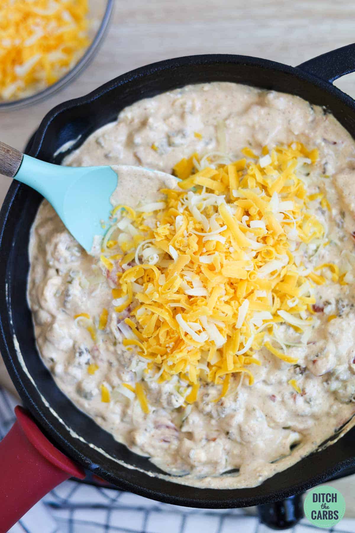 Mixing the shredded cheese into the keto queso dip a little at a time.