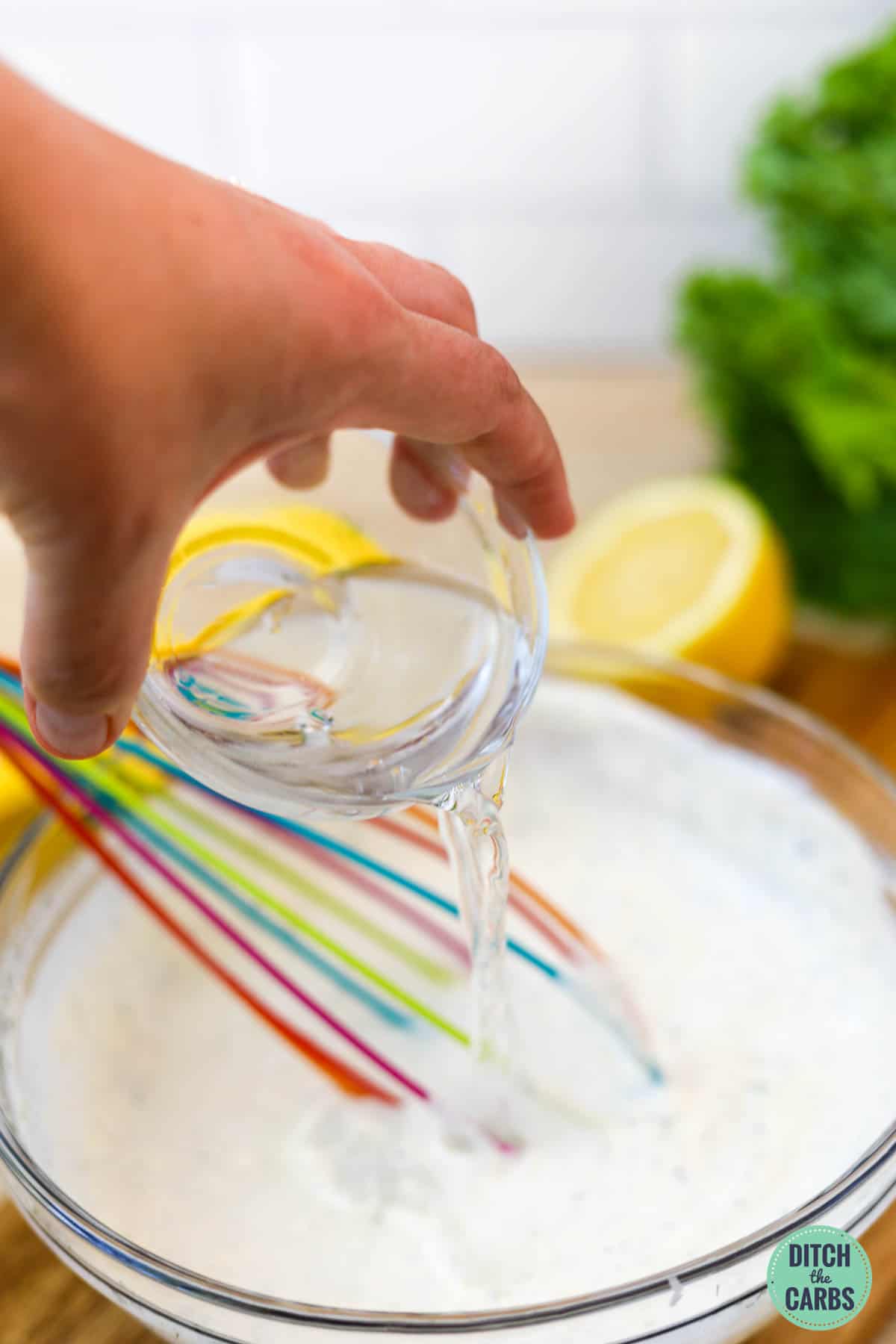 A hand pouring water into keto ranch dressing to thin it out.
