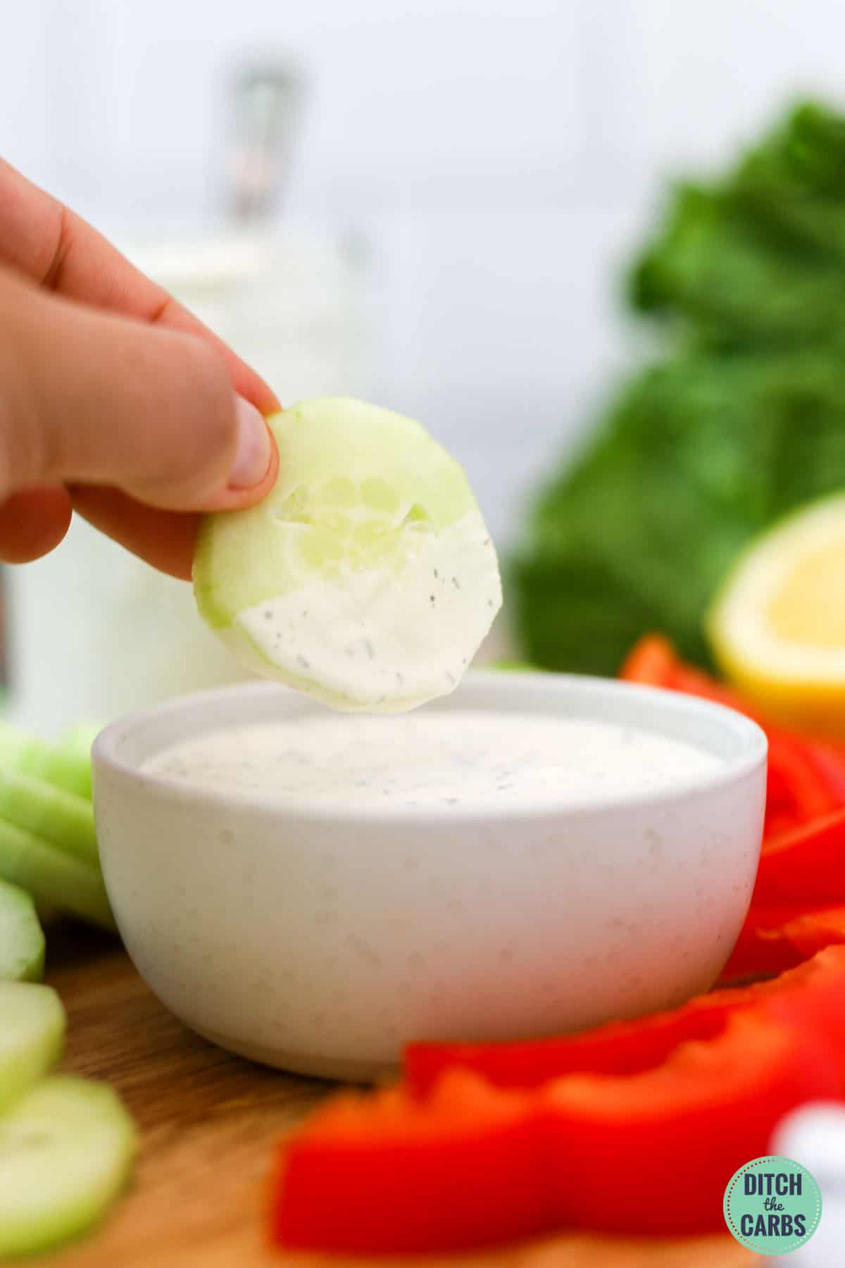A hand dipping a slice of cucumber into the keto ranch dip.