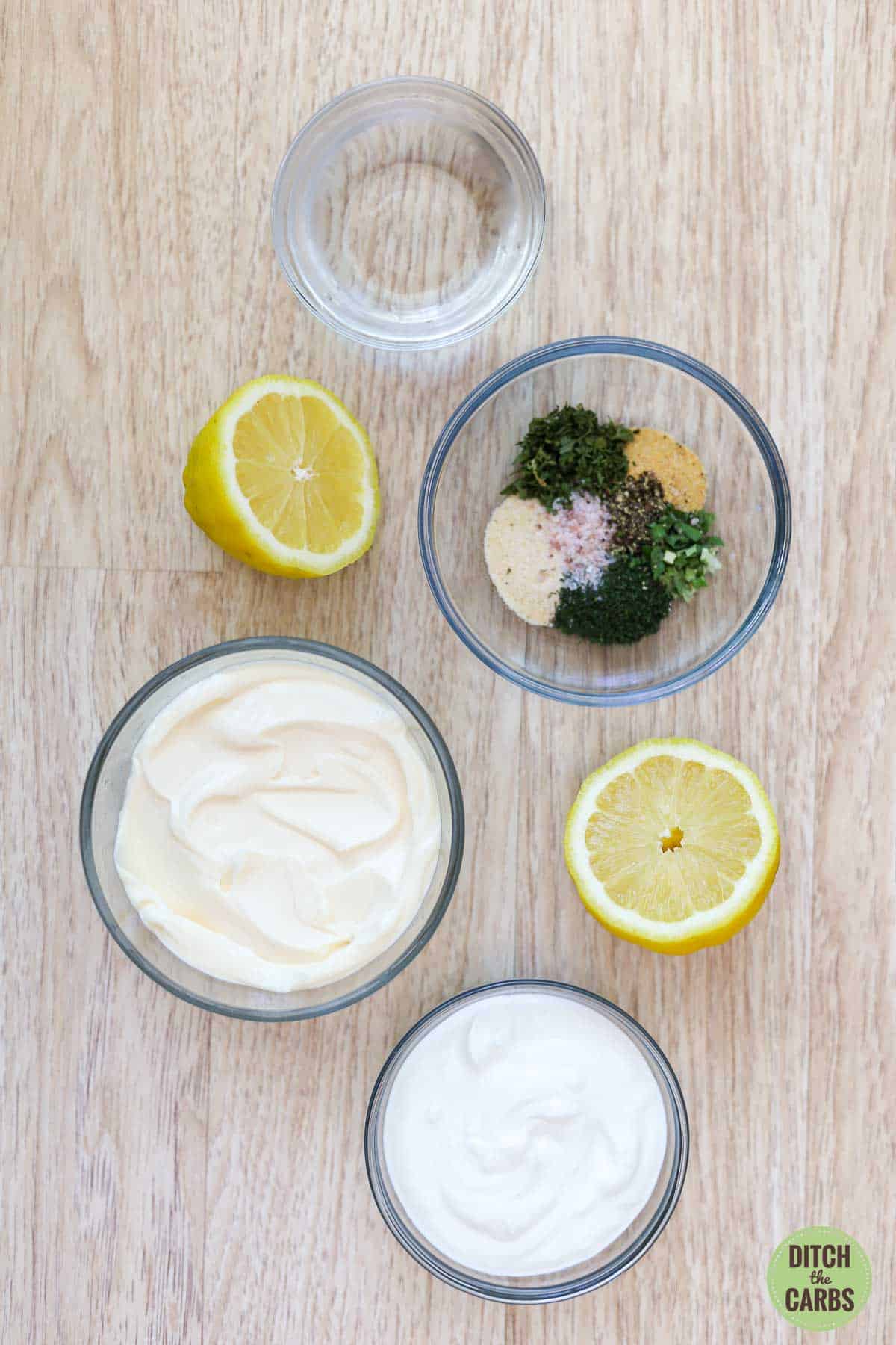 All the ingredients needed to make keto ranch dressing in measured and placed in clear glass bowls on the counter.