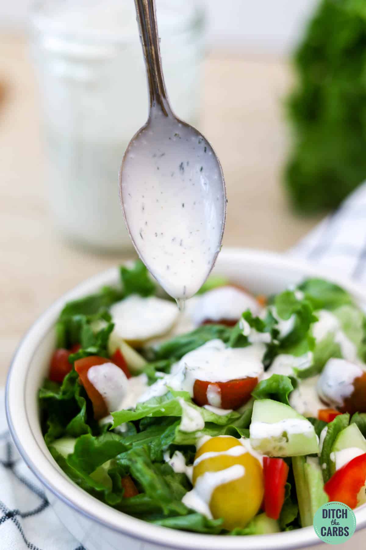 A spoon drizzling keto ranch dressing over a salad.