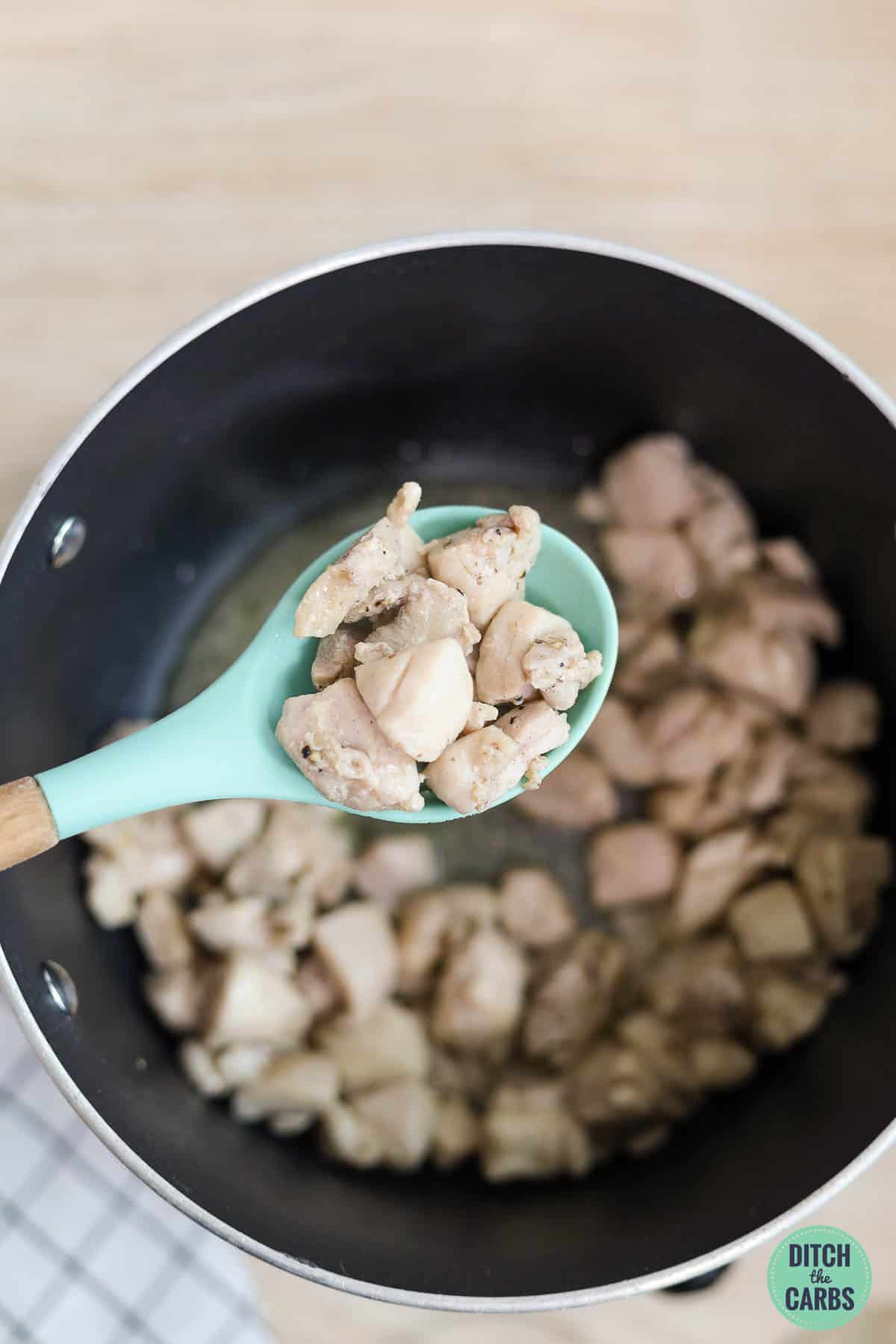A spoon is removing the cooked diced chicken from the pot to be set aside.